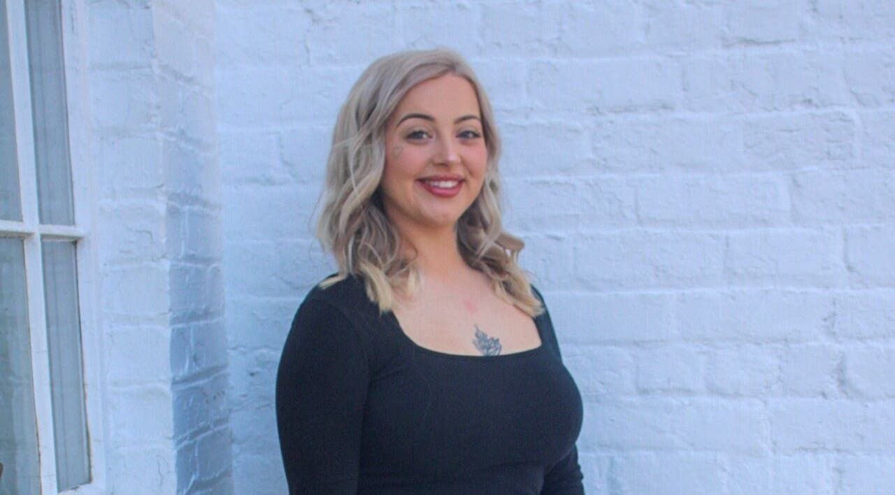 Experienced stylist at So Kno Bliss Salon in Knoxville, Tennessee, US stands against a chic white brick wall.