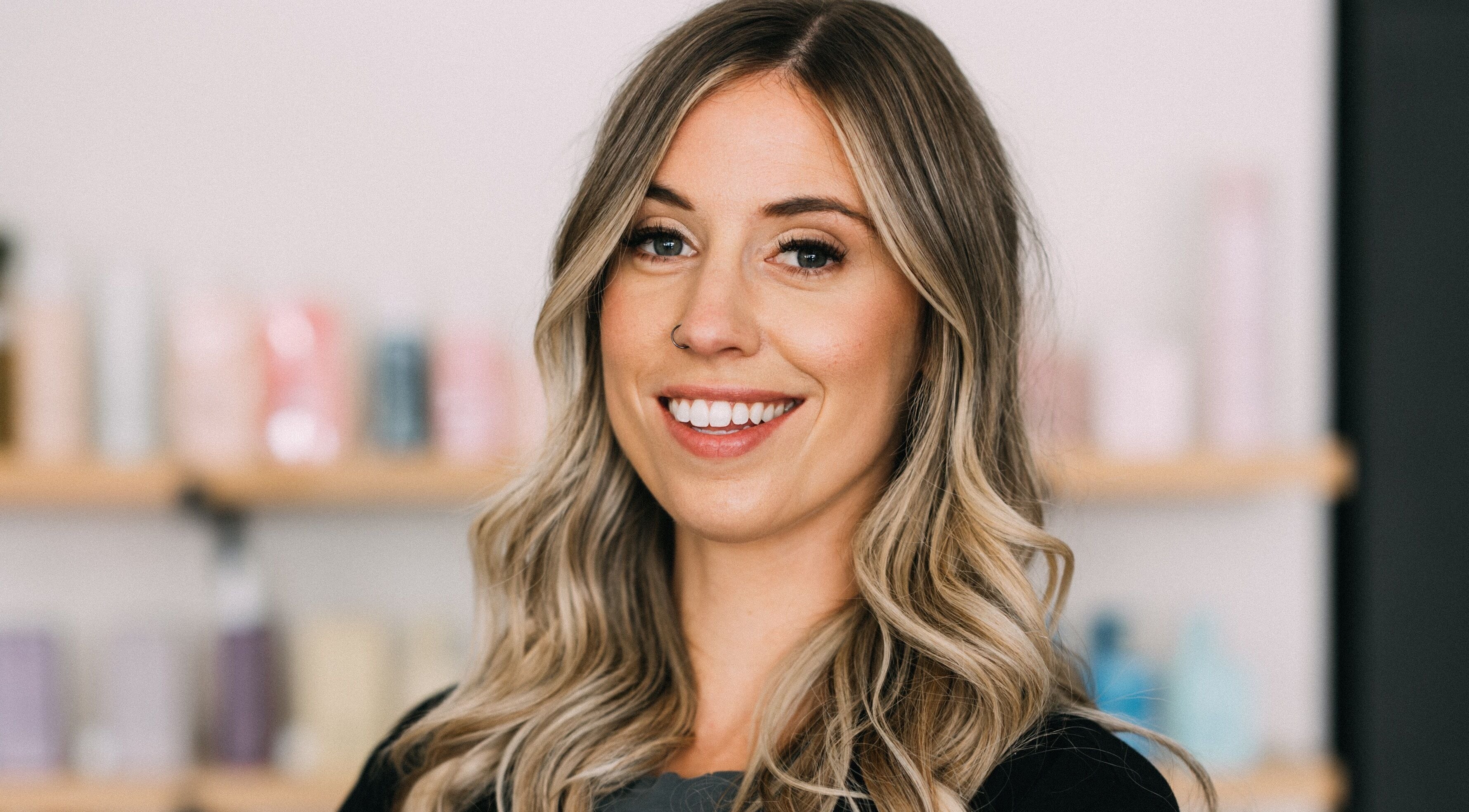 Smiling client at The Hair House, Port Colborne, Ontario, CA, with elegant hairstyling products in background.