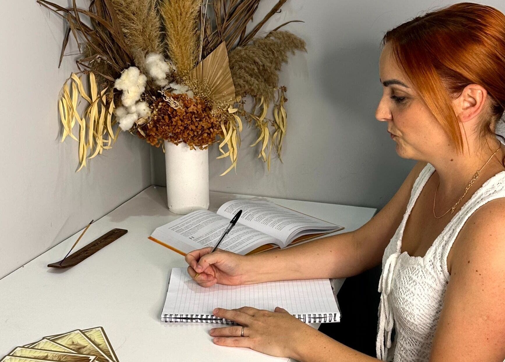 A woman writes at a desk with florals at Balancing Her, Helensvale, Queensland, AU.