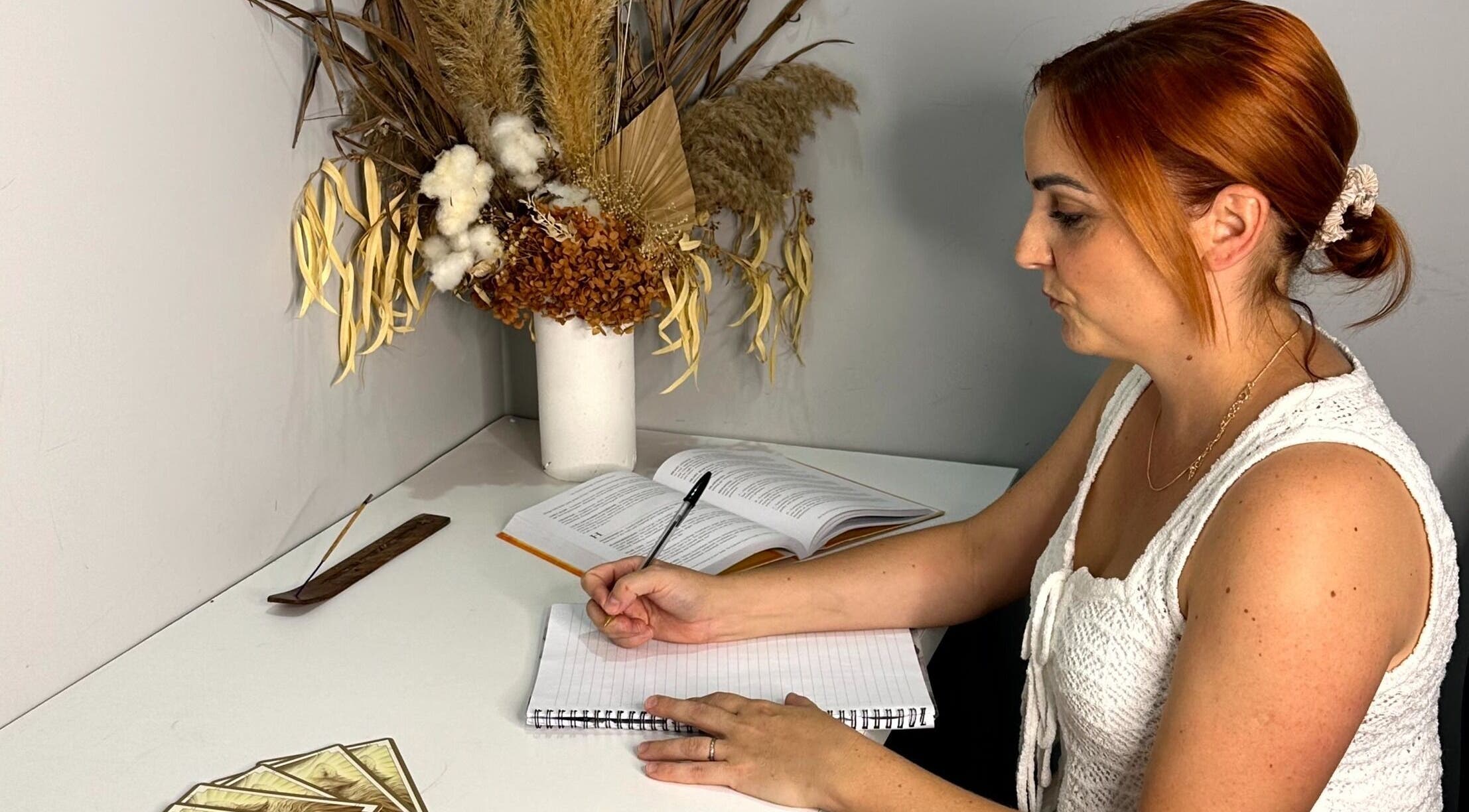 A woman writes at a desk with florals at Balancing Her, Helensvale, Queensland, AU.