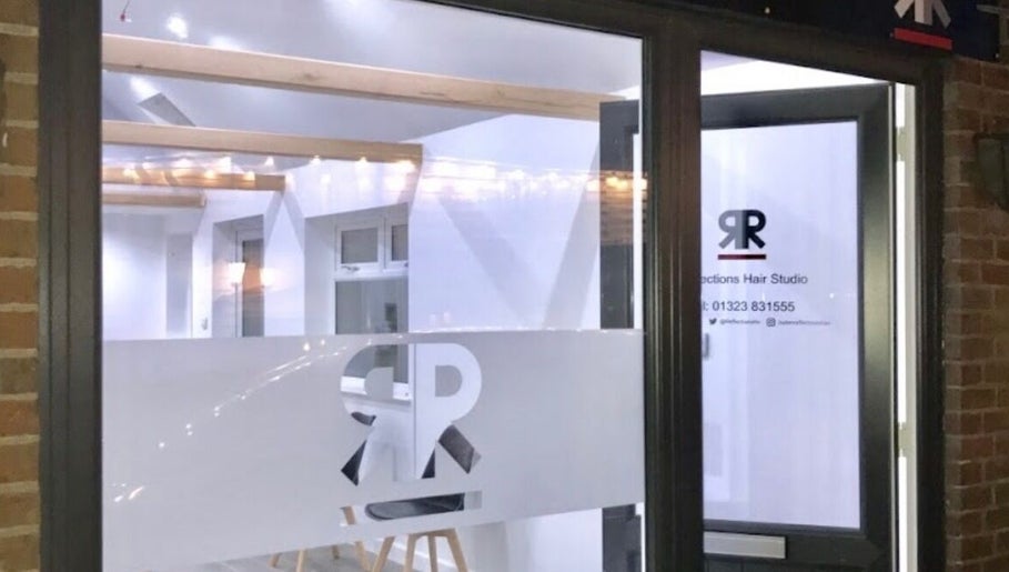 Entrance of Julie at Reflections Hair Studio in Herstmonceux, England, GB at night, with logo on glass.
