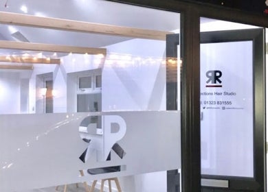 Entrance of Julie at Reflections Hair Studio in Herstmonceux, England, GB at night, with logo on glass.