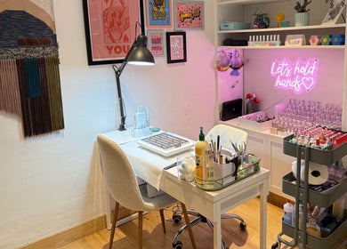 Warm, inviting nail station at Queen B Nail Artistry, London, England, GB with pink neon signs and colorful decor.