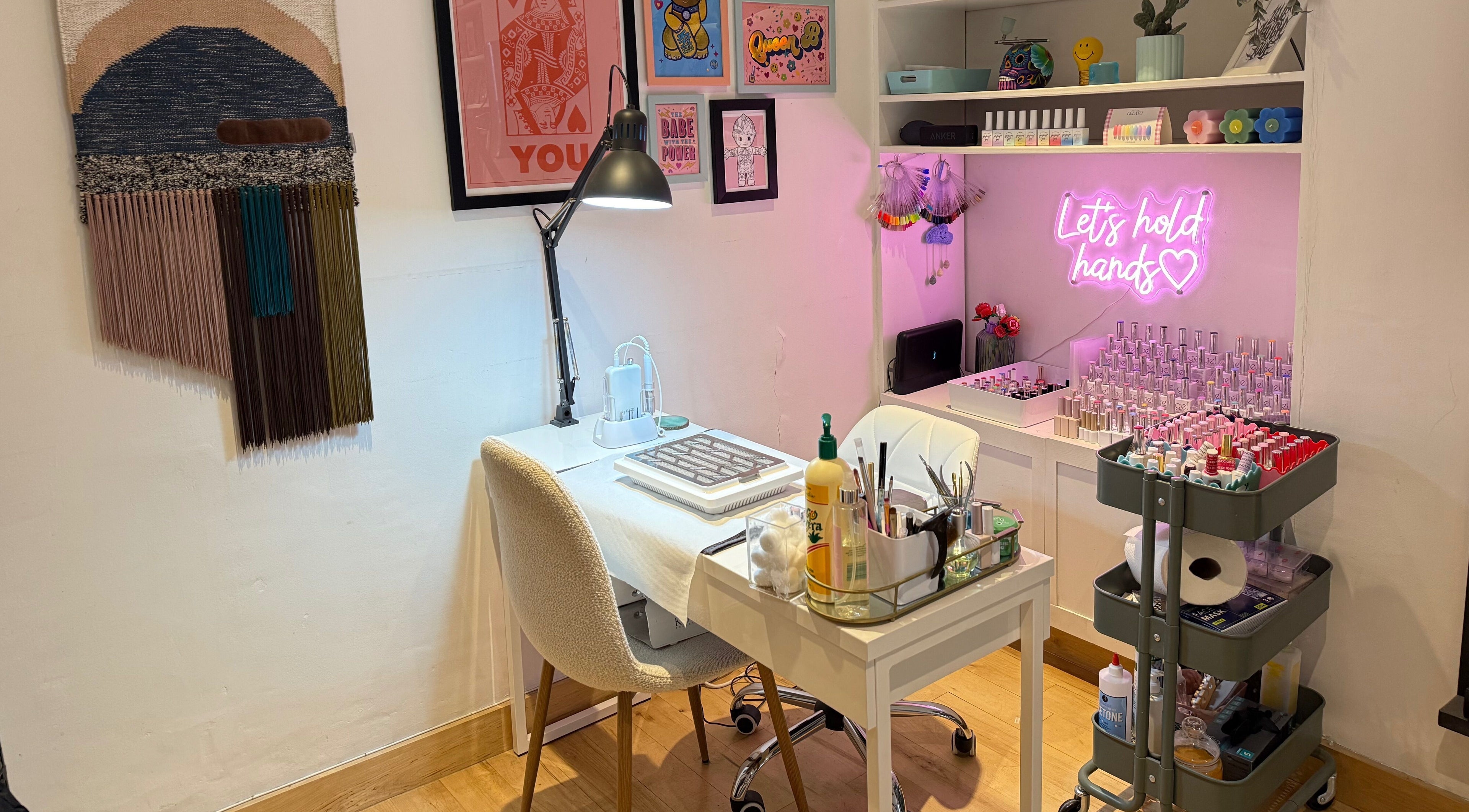 Warm, inviting nail station at Queen B Nail Artistry, London, England, GB with pink neon signs and colorful decor.