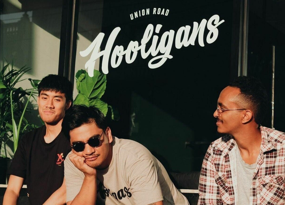 Relaxed trio enjoy sunny ambiance at Be Good Studio, Melbourne, Victoria, AU, surrounded by greenery.