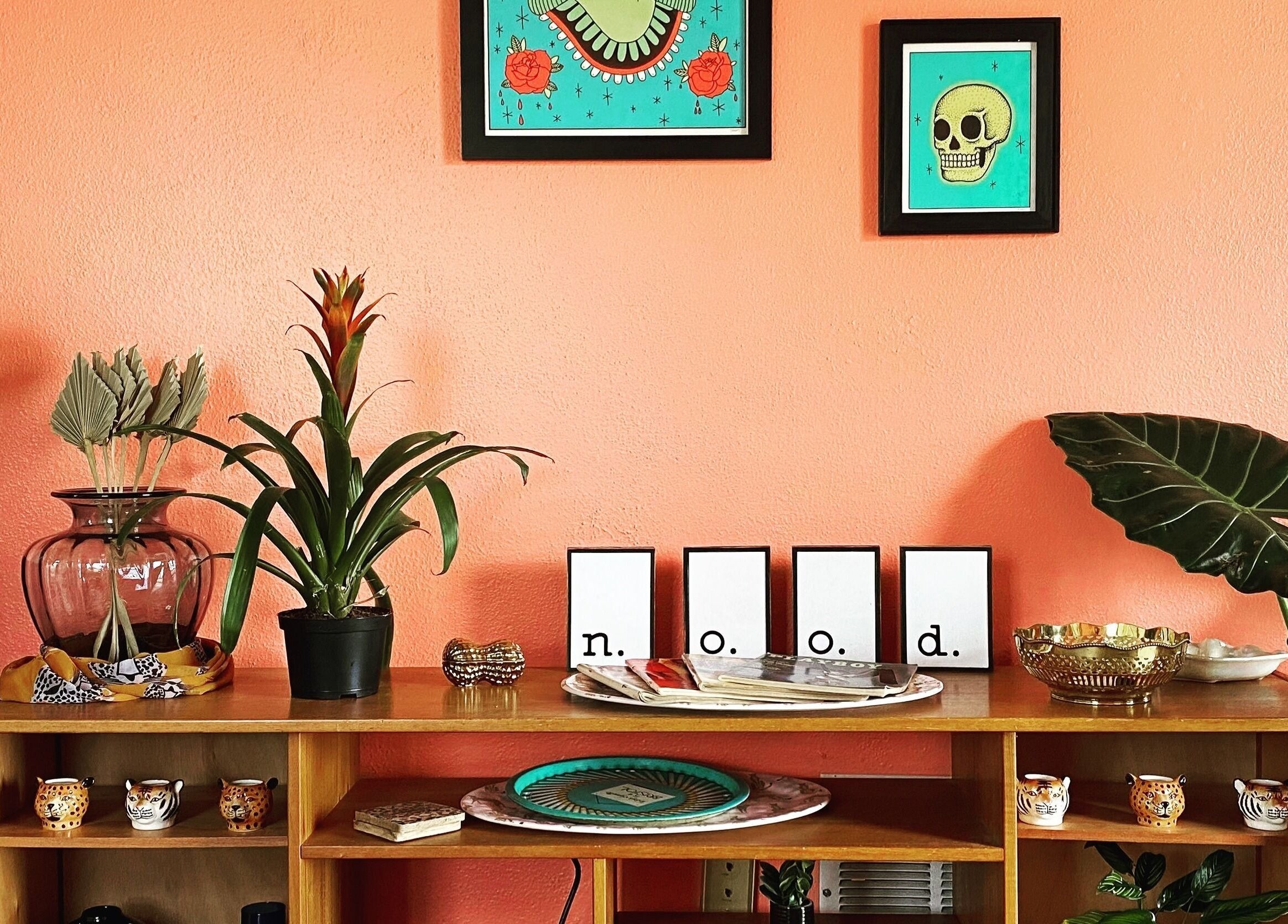 Artistic decor at Nood Wax & Sugar ATX, Austin, Texas, US. Vibrant orange wall with framed art and green plants.