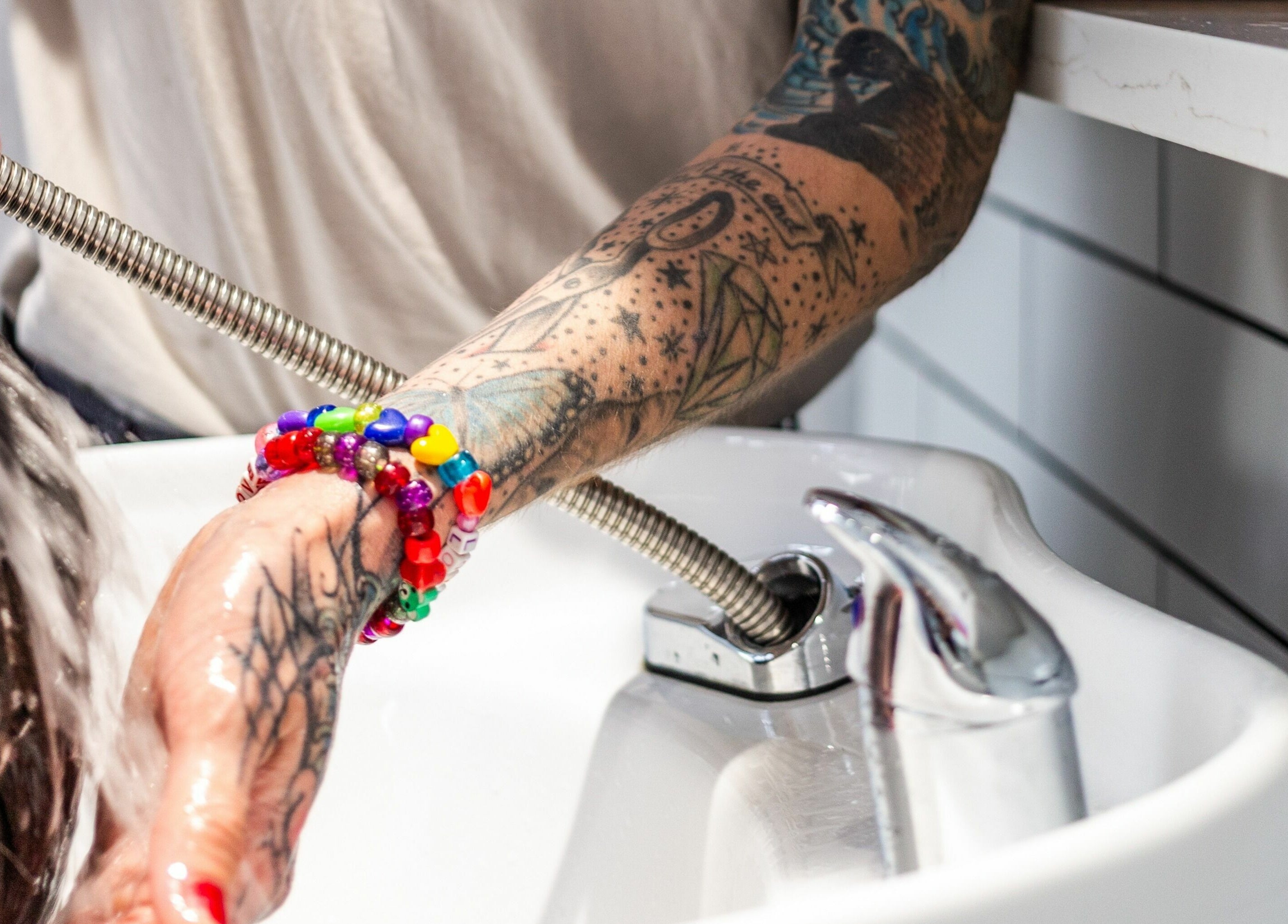 Tattooed stylist washing hair at Rebel X, Calgary, Alberta, CA. Vibrant bracelets add flair to salon service.