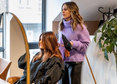 Stylist drying hair at Somewhere in Queens Park, London, England, GB. Modern salon interior with mirrors and plants.