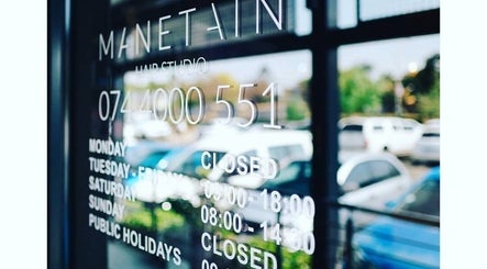 Manetain salon's operational hours displayed on window in Pretoria, Gauteng, ZA with cars reflected outside.