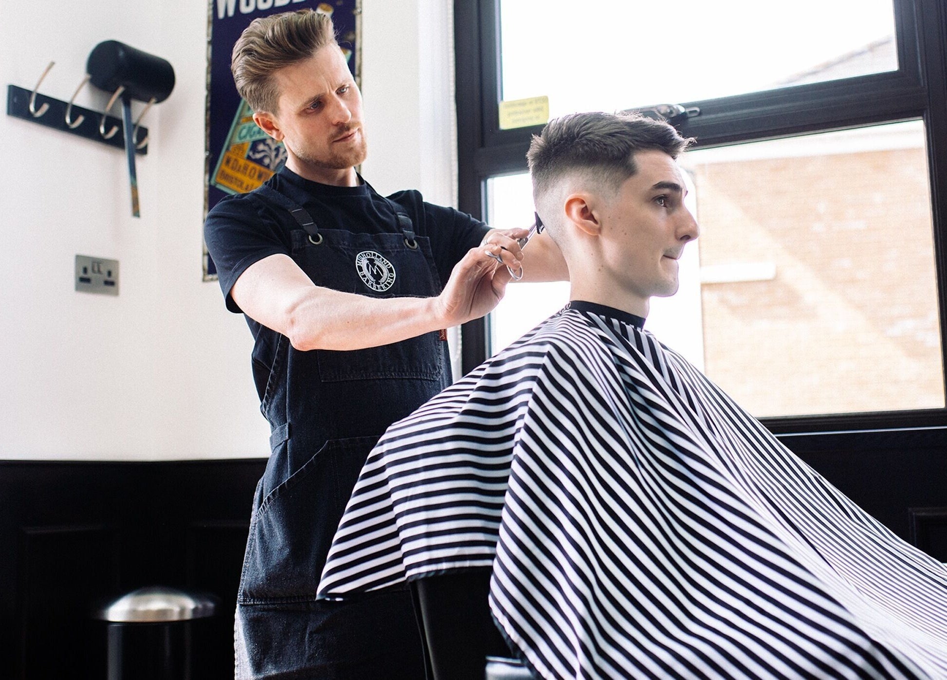 John at Mulholland Barbering in Portadown, Northern Ireland, GB expertly stylizes a client's hair.