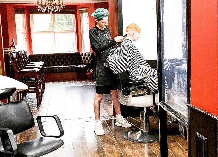 John at Mulholland Barbering in Portadown, Northern Ireland, GB shaping a client's hair in a stylish salon.