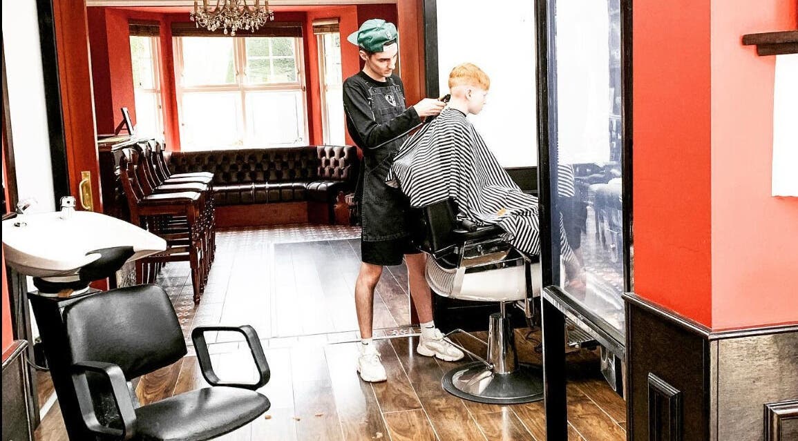 John at Mulholland Barbering in Portadown, Northern Ireland, GB shaping a client's hair in a stylish salon.