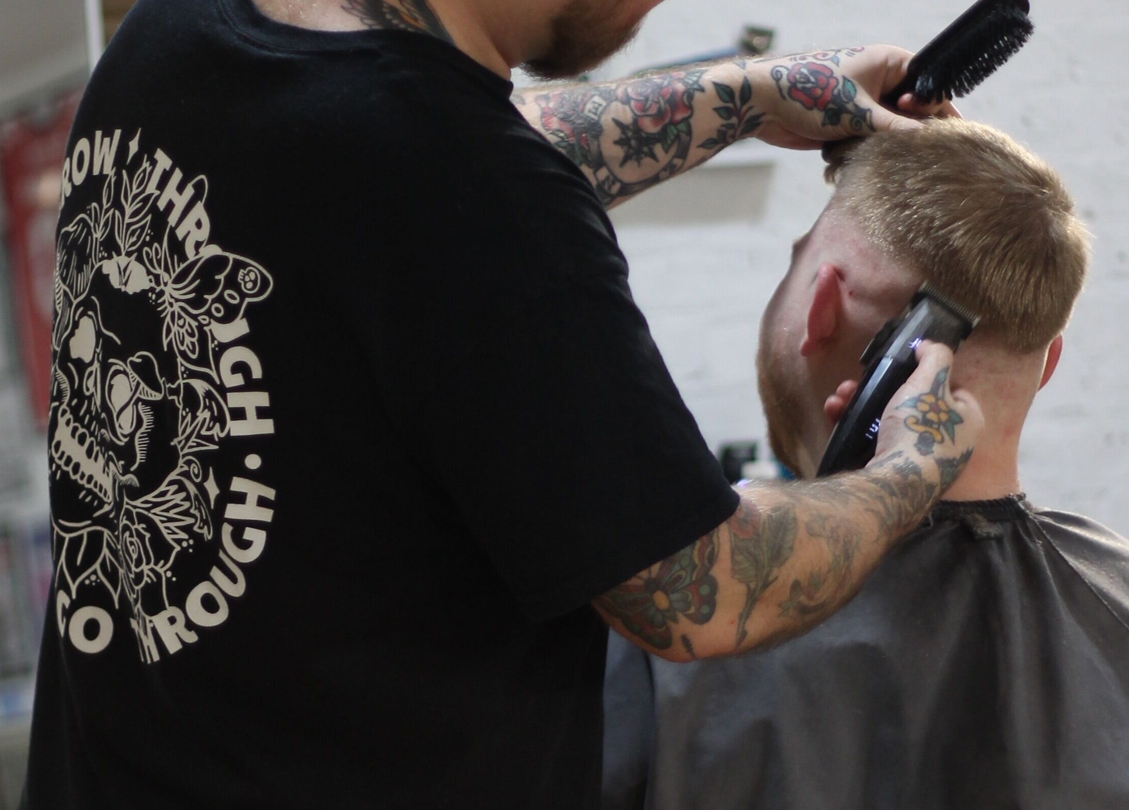 Barber at No Bad Days in Rochester, England, GB, giving a haircut with tattoos visible.