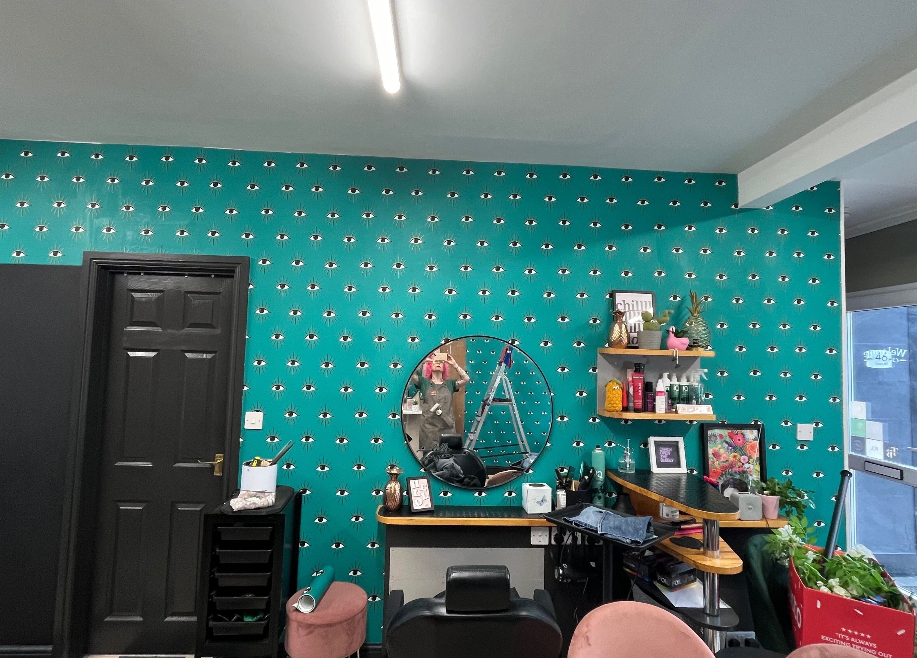 Trendy salon interior at Trim in Stafford, England, GB with a teal eye-patterned wall and stylish decor.