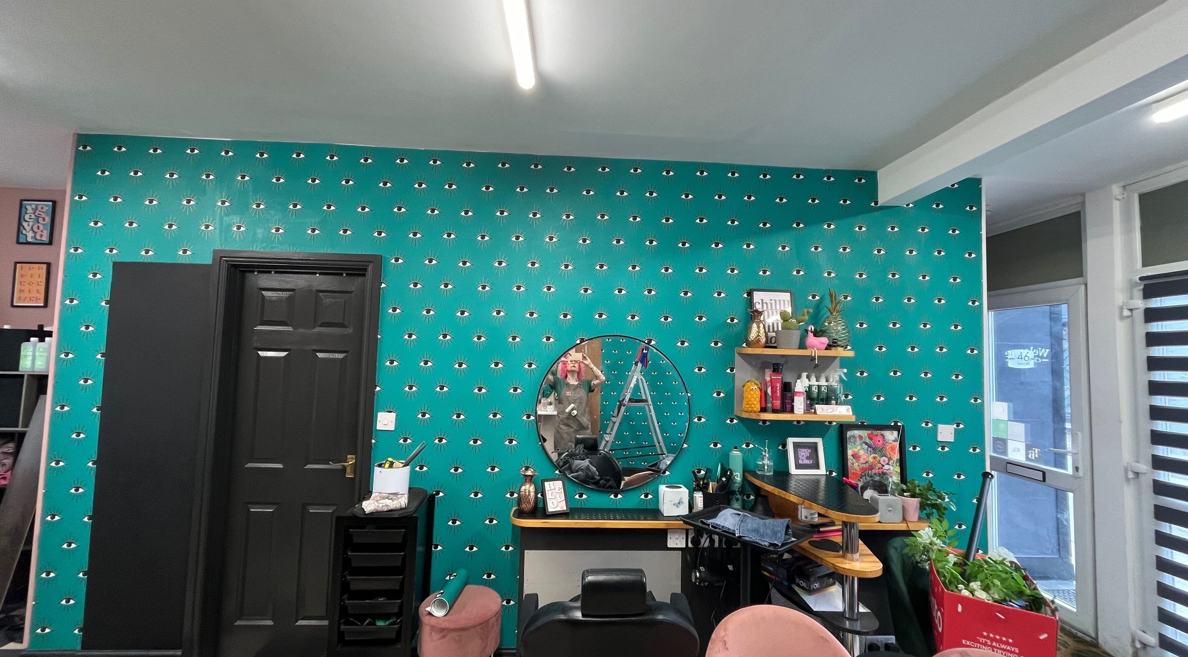 Trendy salon interior at Trim in Stafford, England, GB with a teal eye-patterned wall and stylish decor.