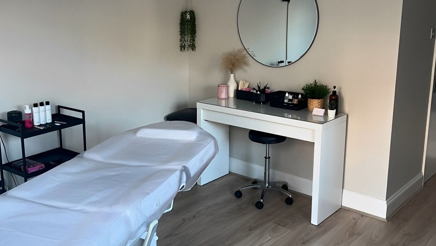 Treatment room at Victoria Alice Brows, Newbury, England, GB. Features massage table and vanity with round mirror.