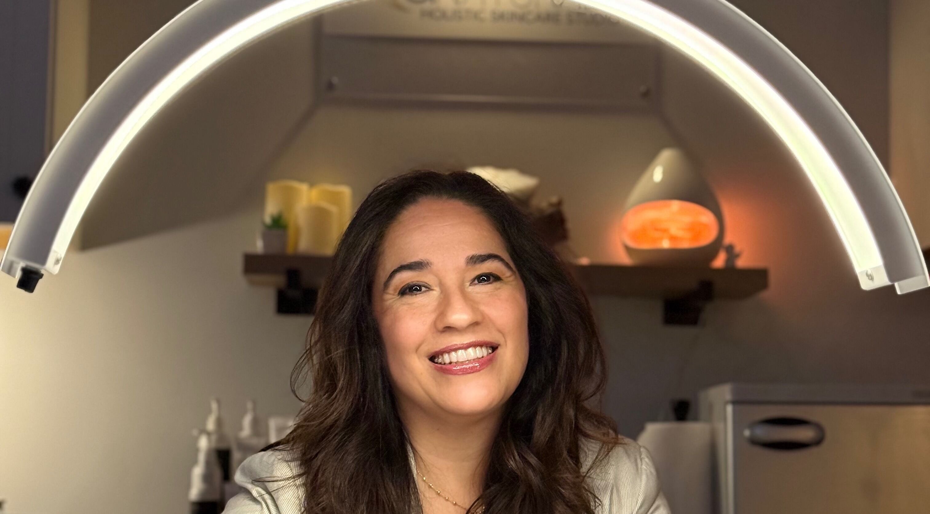 Woman smiling under skincare light at ANATURALE HOLISTIC SKINCARE STUDIO, Henrico, Virginia, US.