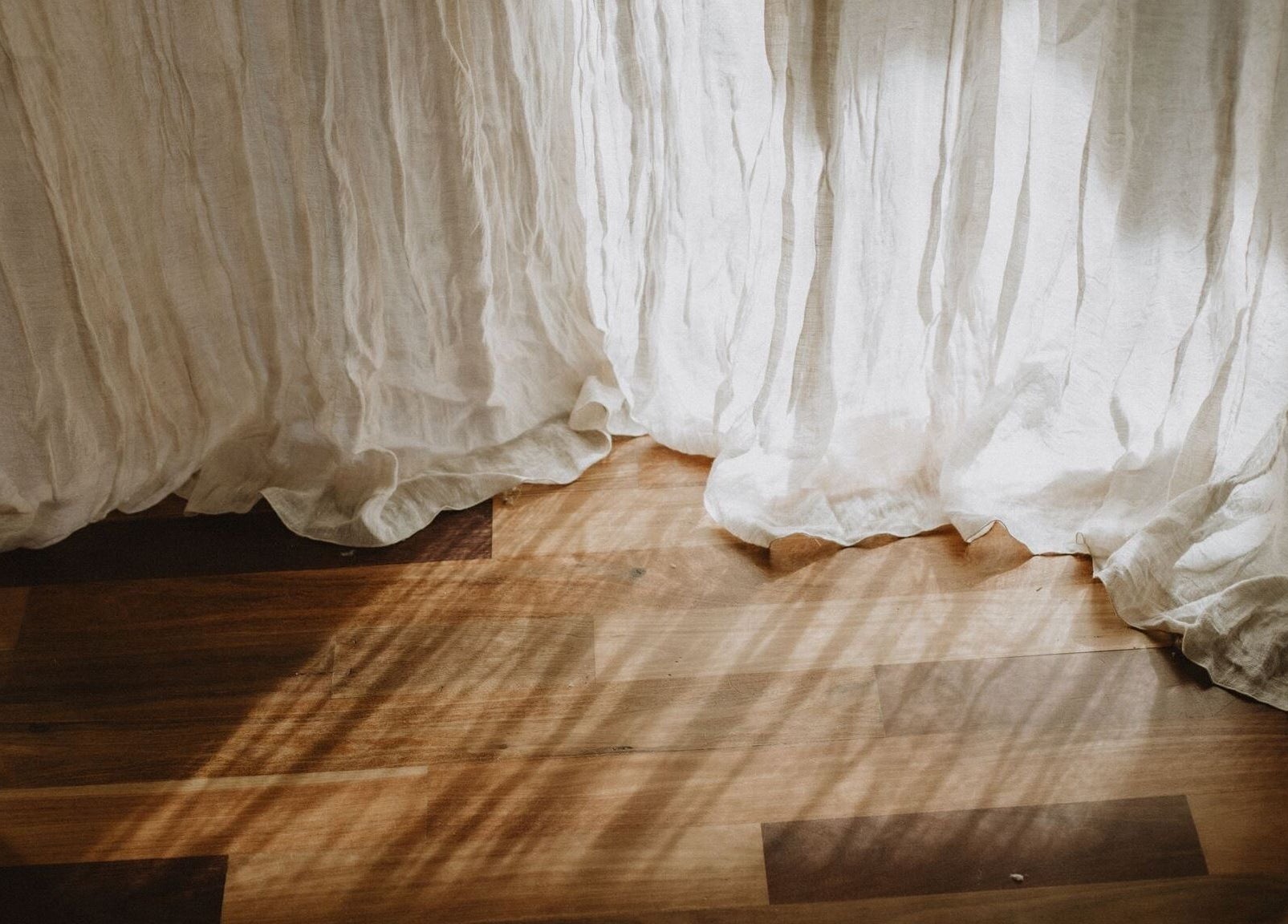 Sunlit white curtain flowing over wooden floor at UMICA, Byron Bay, New South Wales, AU.