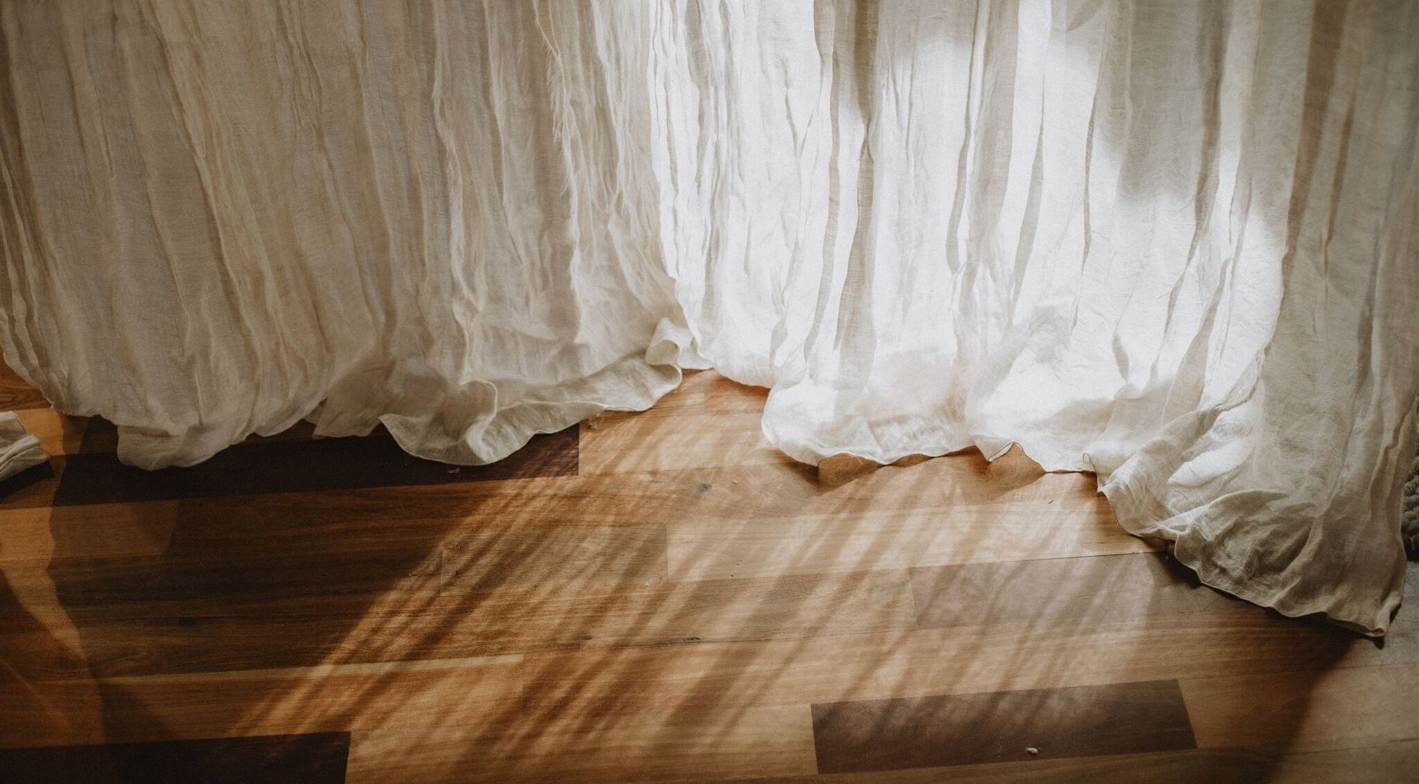 Sunlit white curtain flowing over wooden floor at UMICA, Byron Bay, New South Wales, AU.