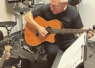 Music lesson at Michael Prizeman Music School, Melbourne, Victoria, AU with teacher and student playing guitar.