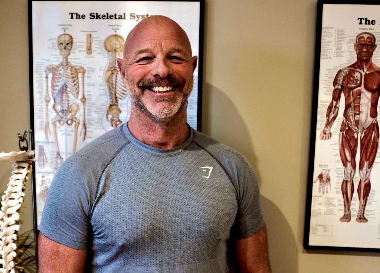 Therapist at Alpha Massage - Chobham Clinic in Chobham, England, GB, standing beside anatomical charts.