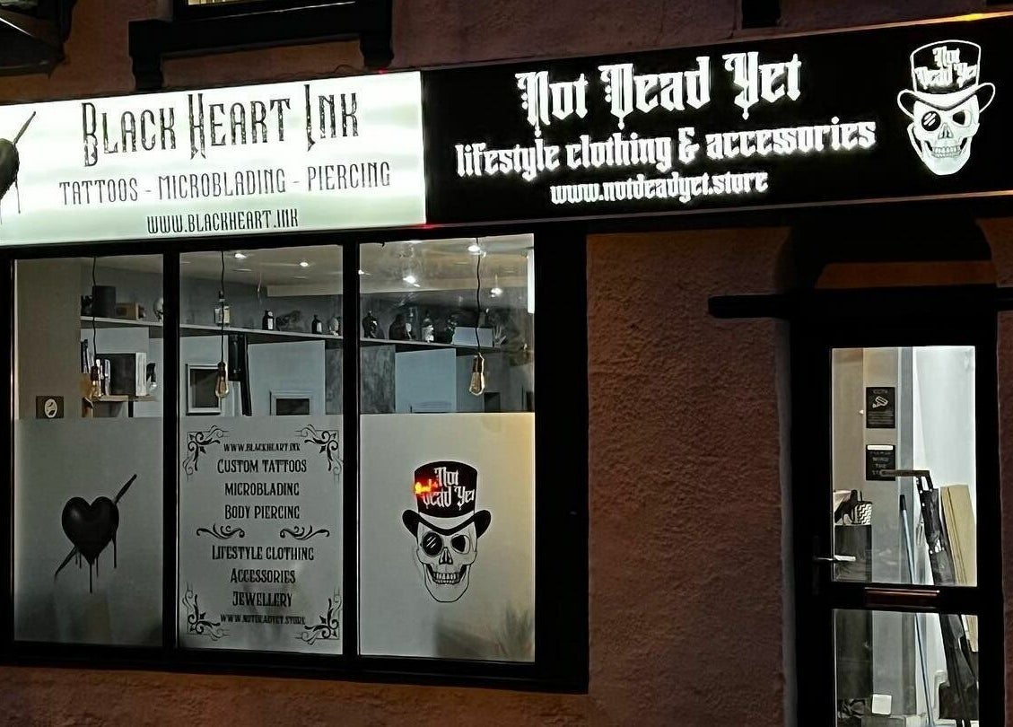 Exterior of Black Heart Ink, a tattoo and piercing studio in Swindon, England, GB, showcasing signage at night.