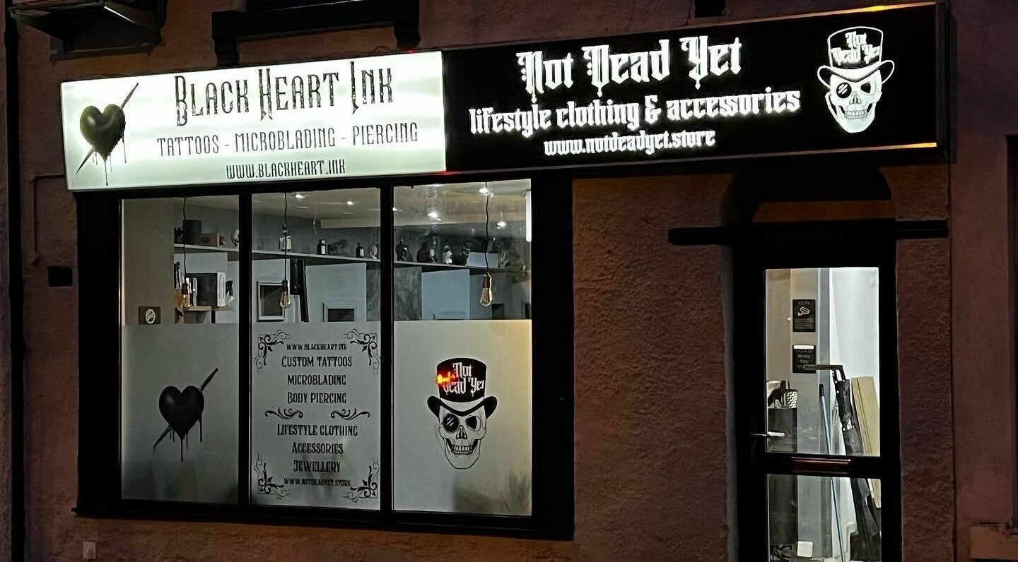 Exterior of Black Heart Ink, a tattoo and piercing studio in Swindon, England, GB, showcasing signage at night.