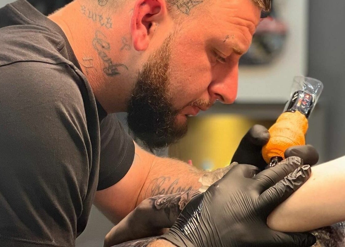 Artist creating a tattoo at Black Heart Ink, Swindon, England, GB, detailing ink work on client's arm.