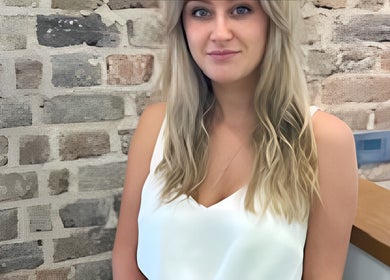 A woman in Alice Ellen Hairdressing, Portslade, England, GB, stands in front of a stylish stone wall.
