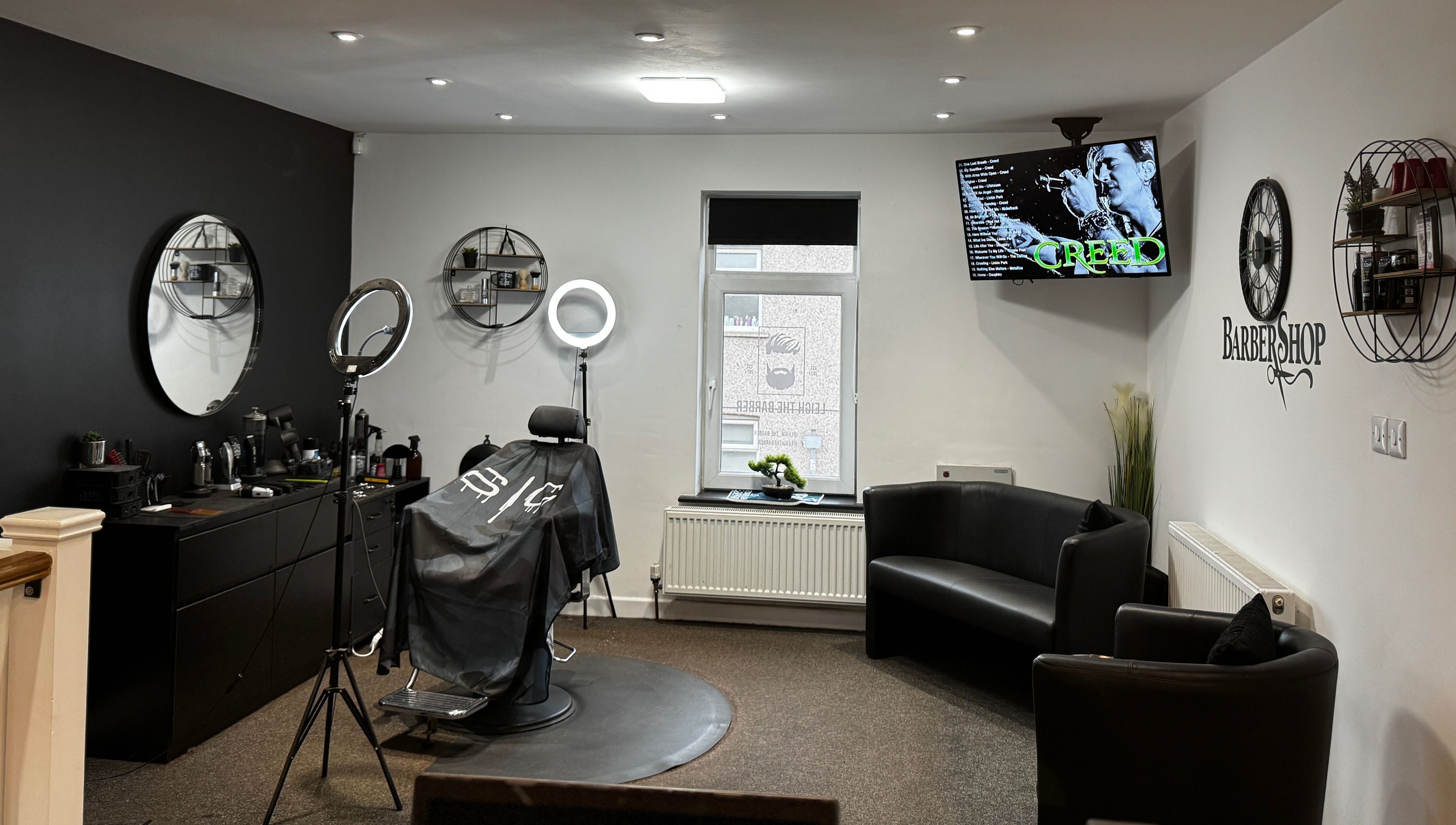 Leigh the Barber's stylish interior in Barrow in Furness, England, GB, showcasing sleek black decor and a cozy seating area.