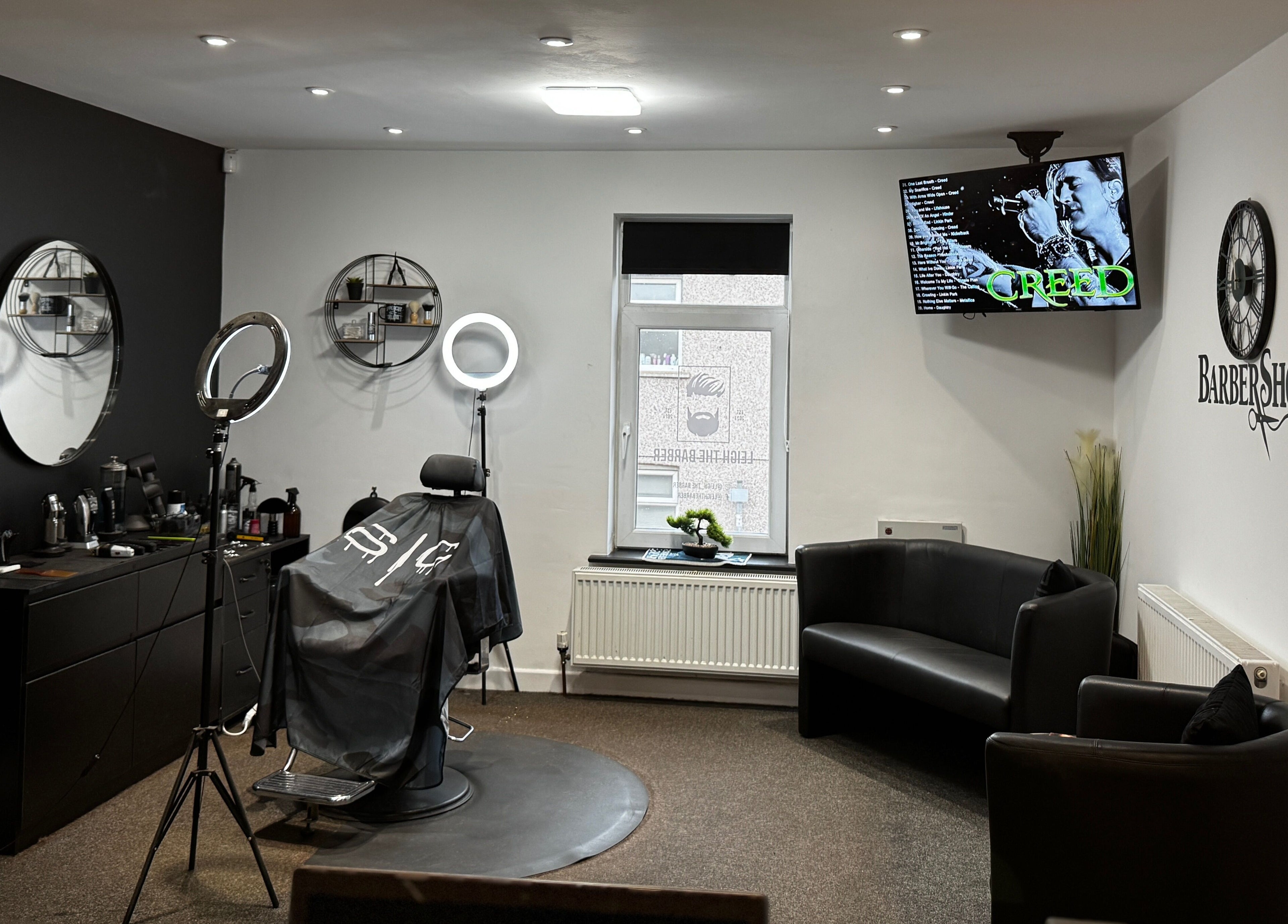 Leigh the Barber's stylish interior in Barrow in Furness, England, GB, showcasing sleek black decor and a cozy seating area.