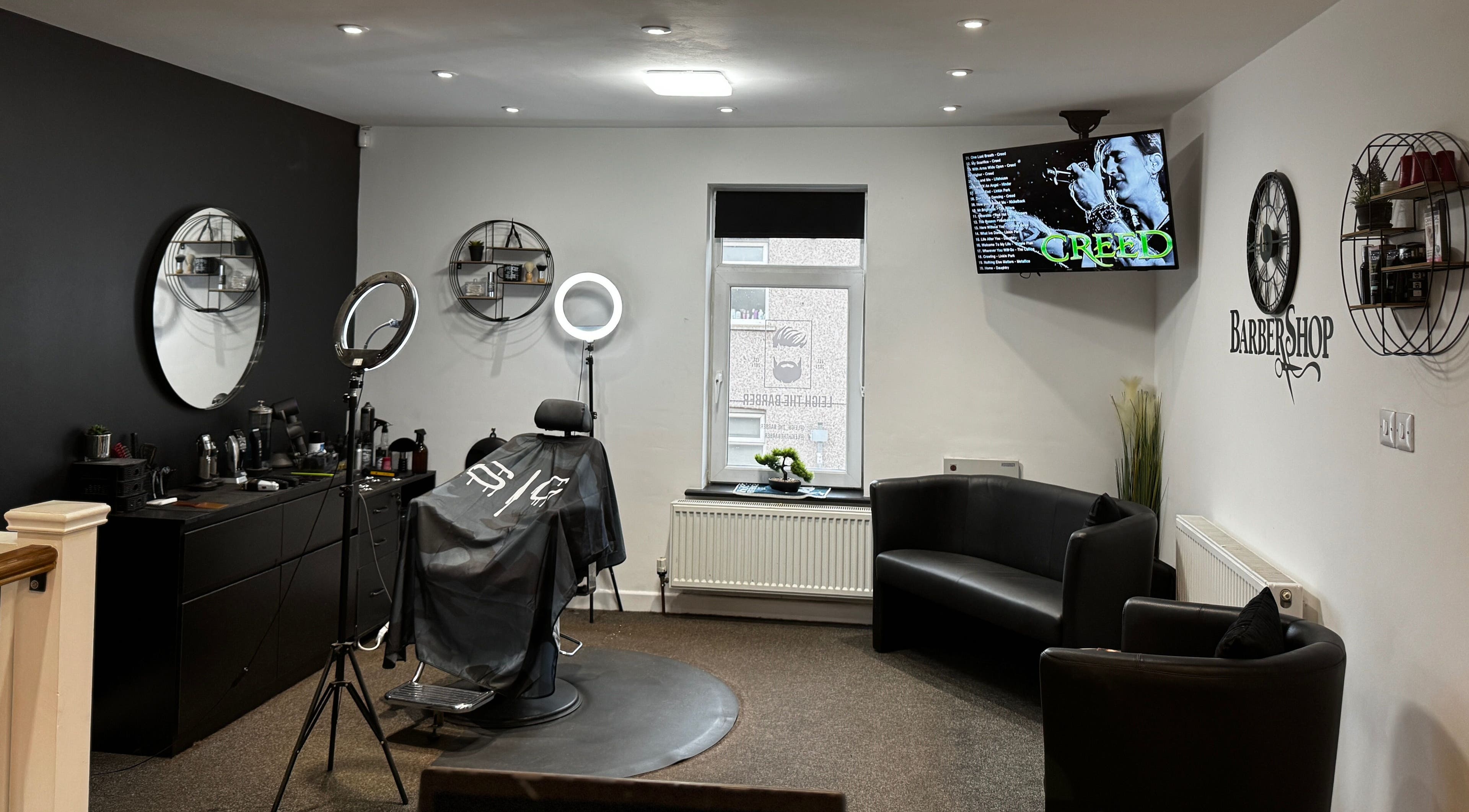 Leigh the Barber's stylish interior in Barrow in Furness, England, GB, showcasing sleek black decor and a cozy seating area.