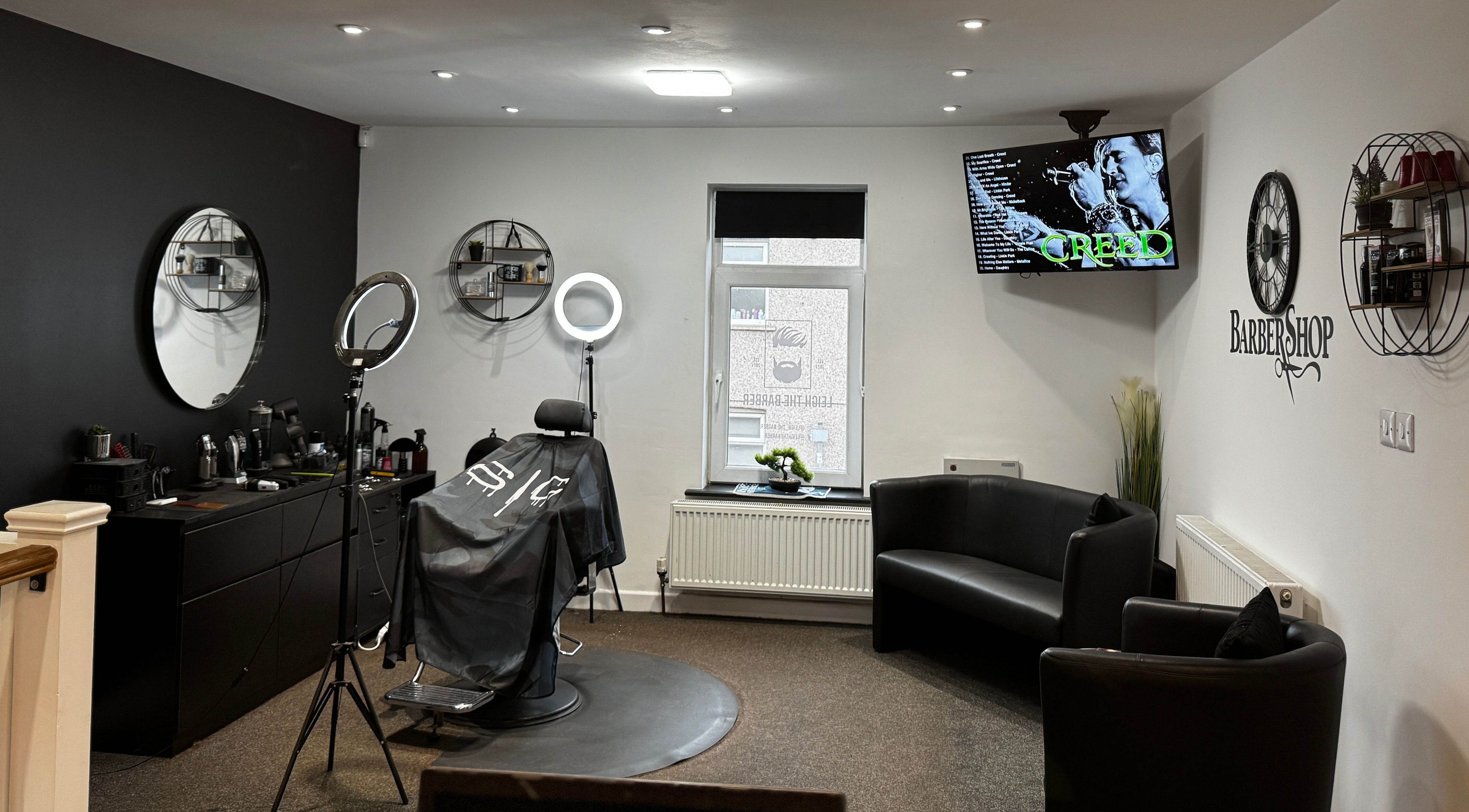Leigh the Barber's stylish interior in Barrow in Furness, England, GB, showcasing sleek black decor and a cozy seating area.
