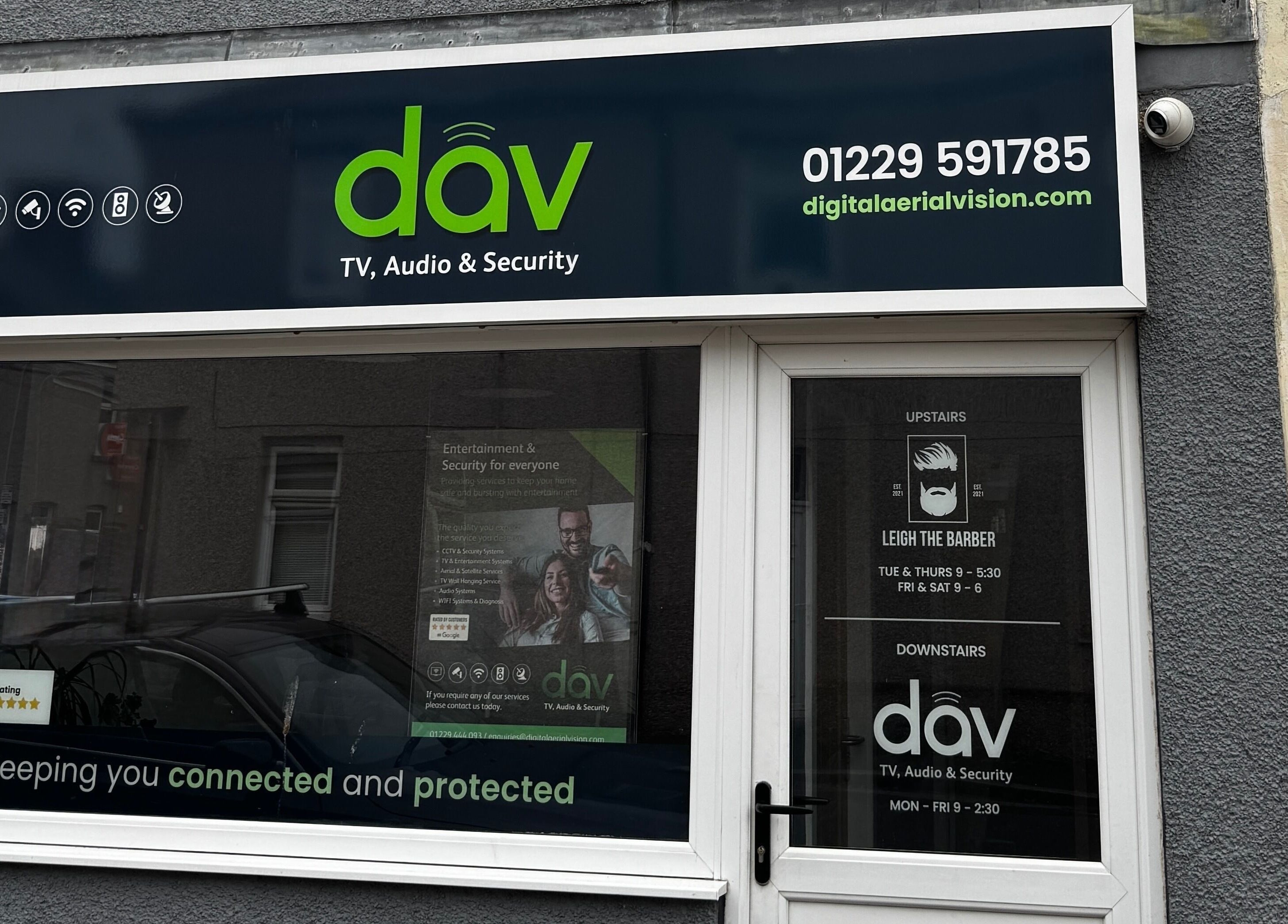 Front window of Leigh the Barber in Barrow in Furness, England, GB, showcasing services and ratings.