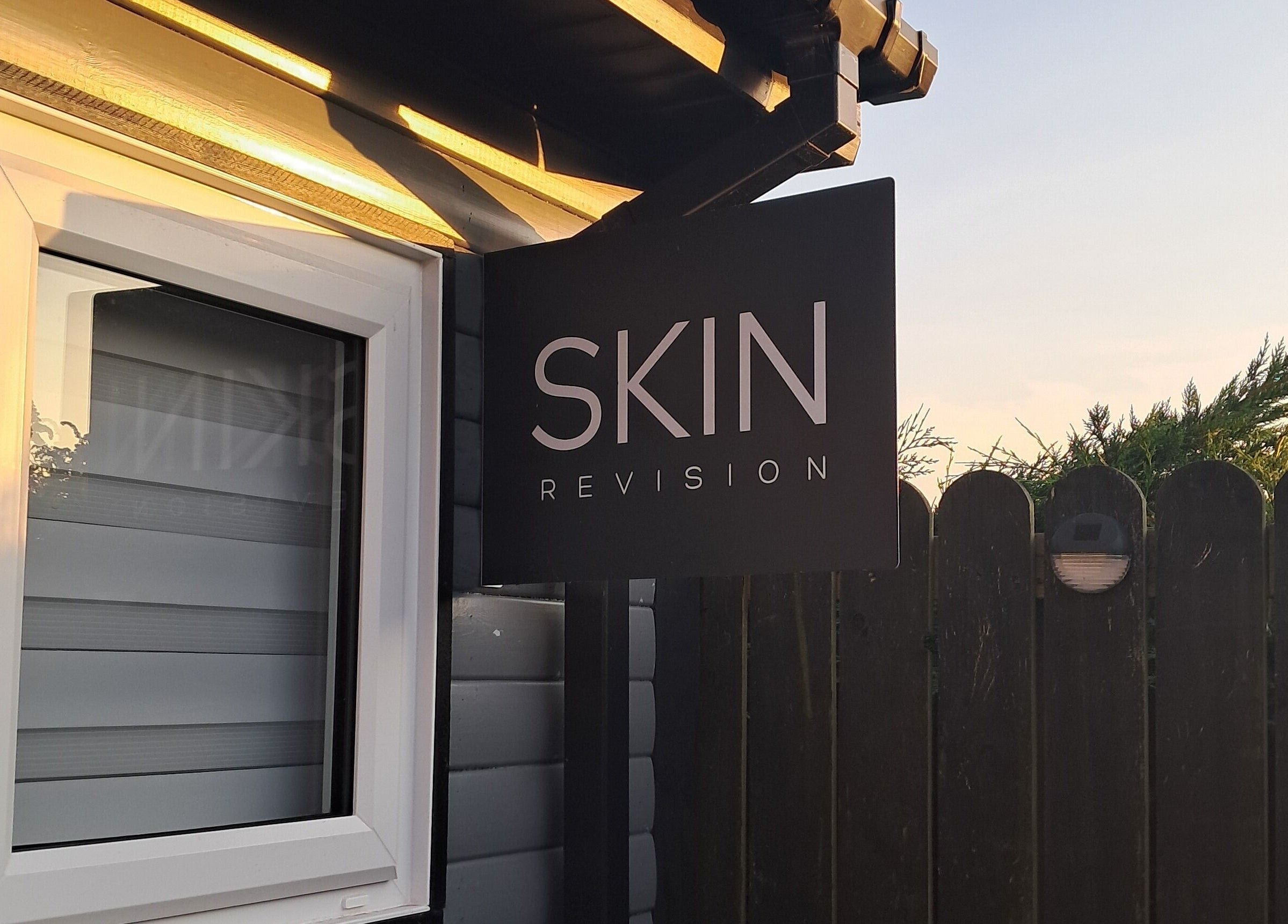 Skin Revision sign in Douglas, IM glowing in sunset light, highlighting beauty venue entrance.
