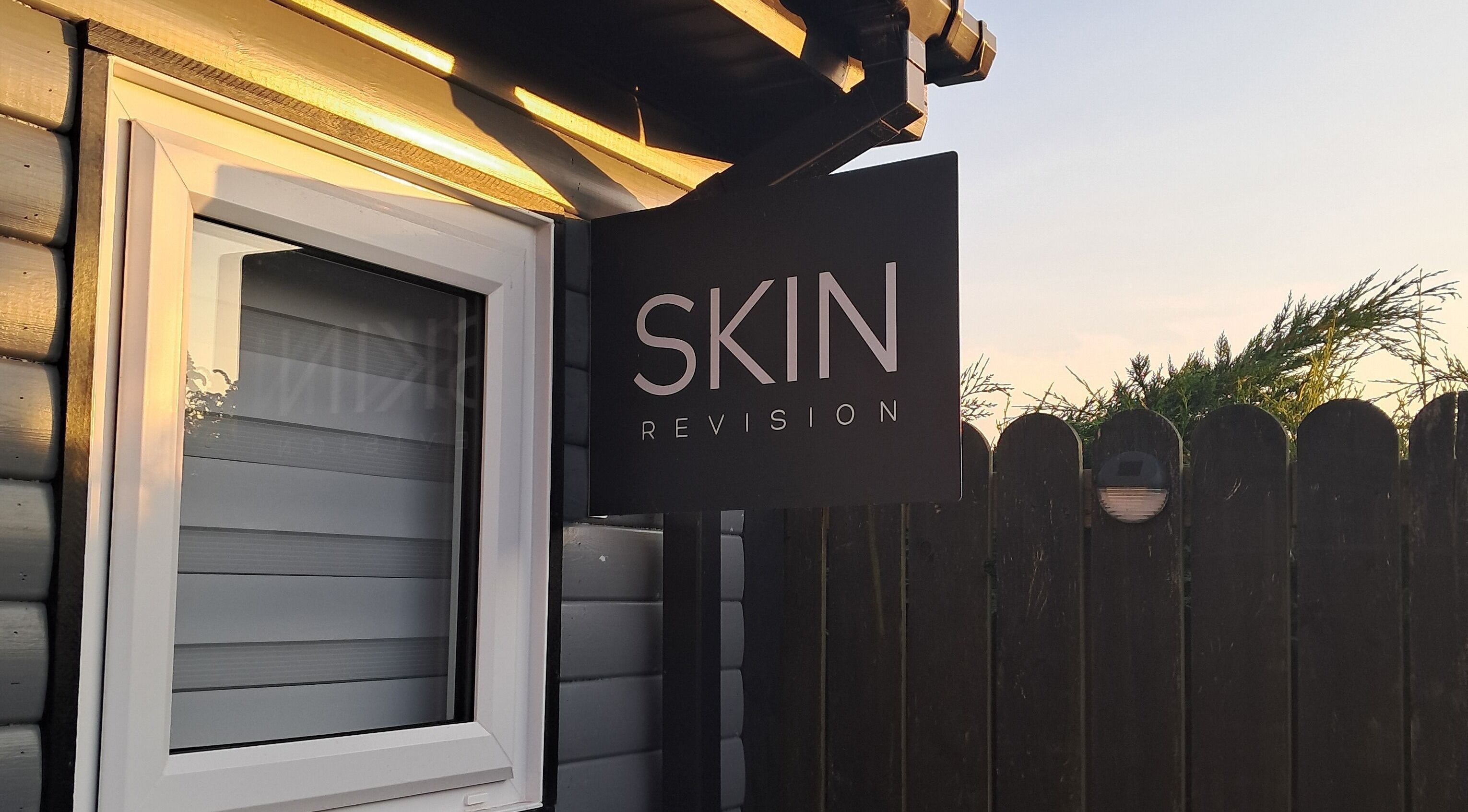 Skin Revision sign in Douglas, IM glowing in sunset light, highlighting beauty venue entrance.