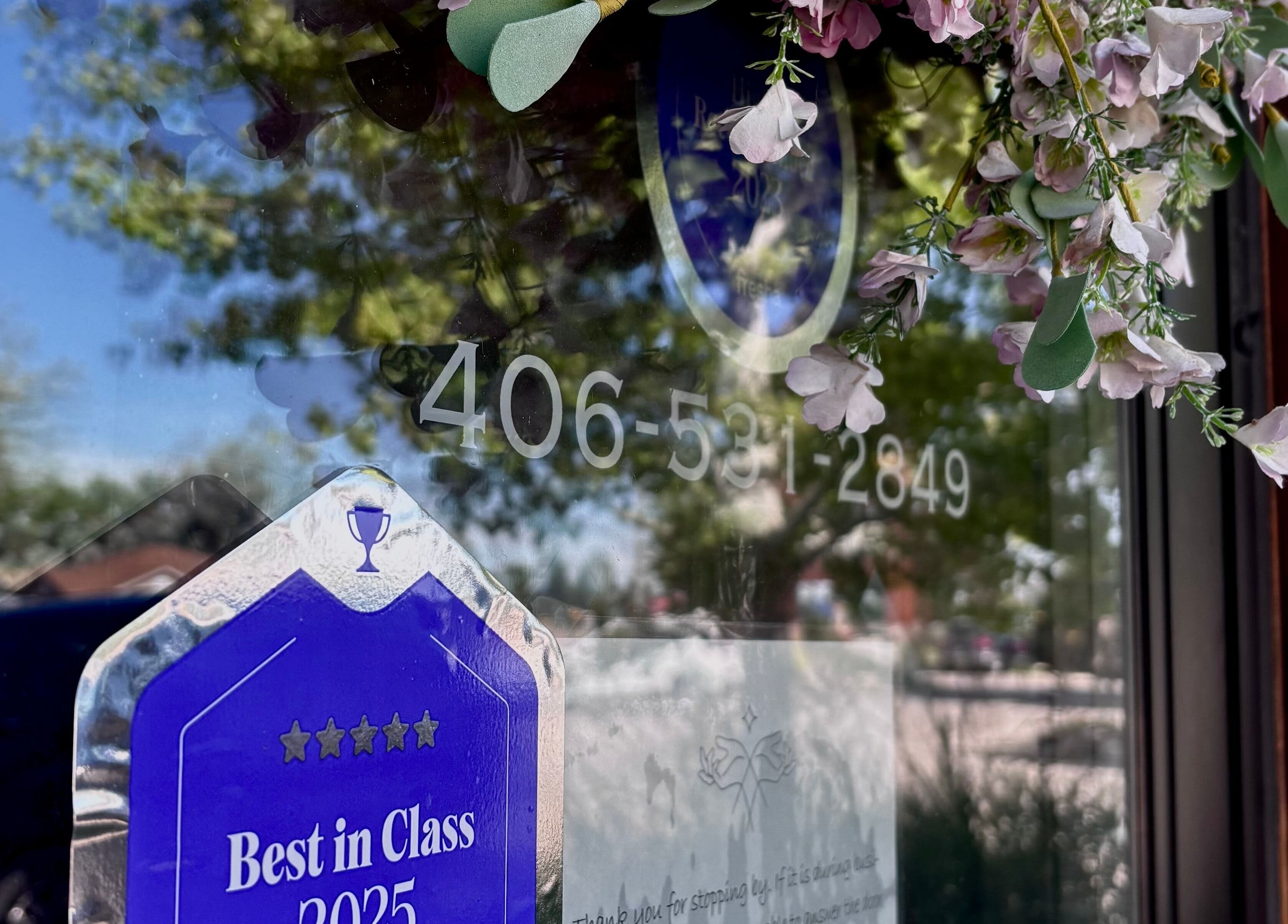 Award sticker on Massage Therapy Studio window in Great Falls, Montana, US adorned with flowers and phone number.