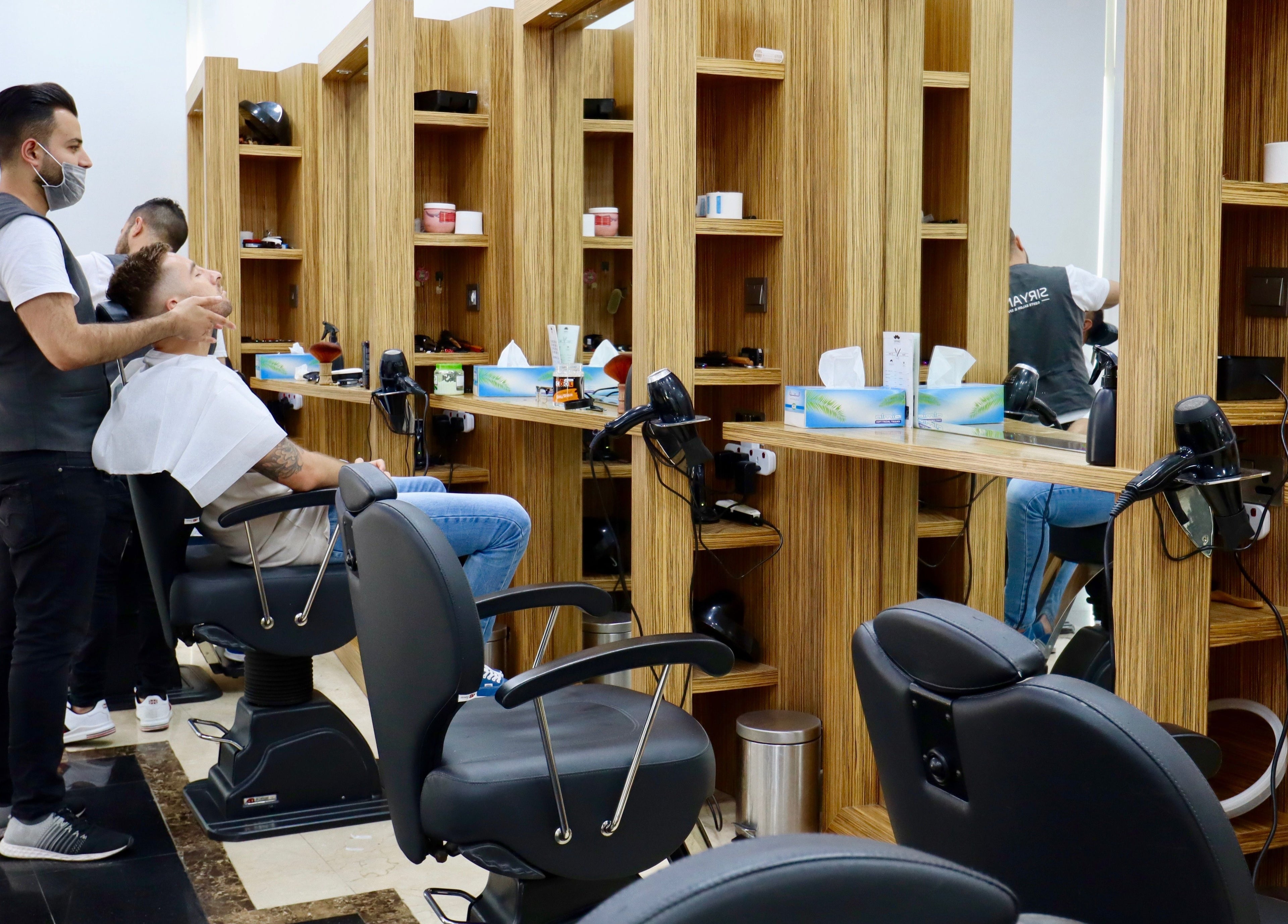Barber servicing client at Siryano Gents Saloon and Spa, Escape Tower, Dubai, AE. Modern interior design.