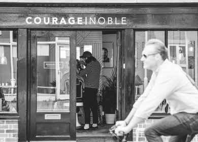 Exterior of Courage Noble | King Street, Norwich, England, GB with a cyclist passing by the barbershop.