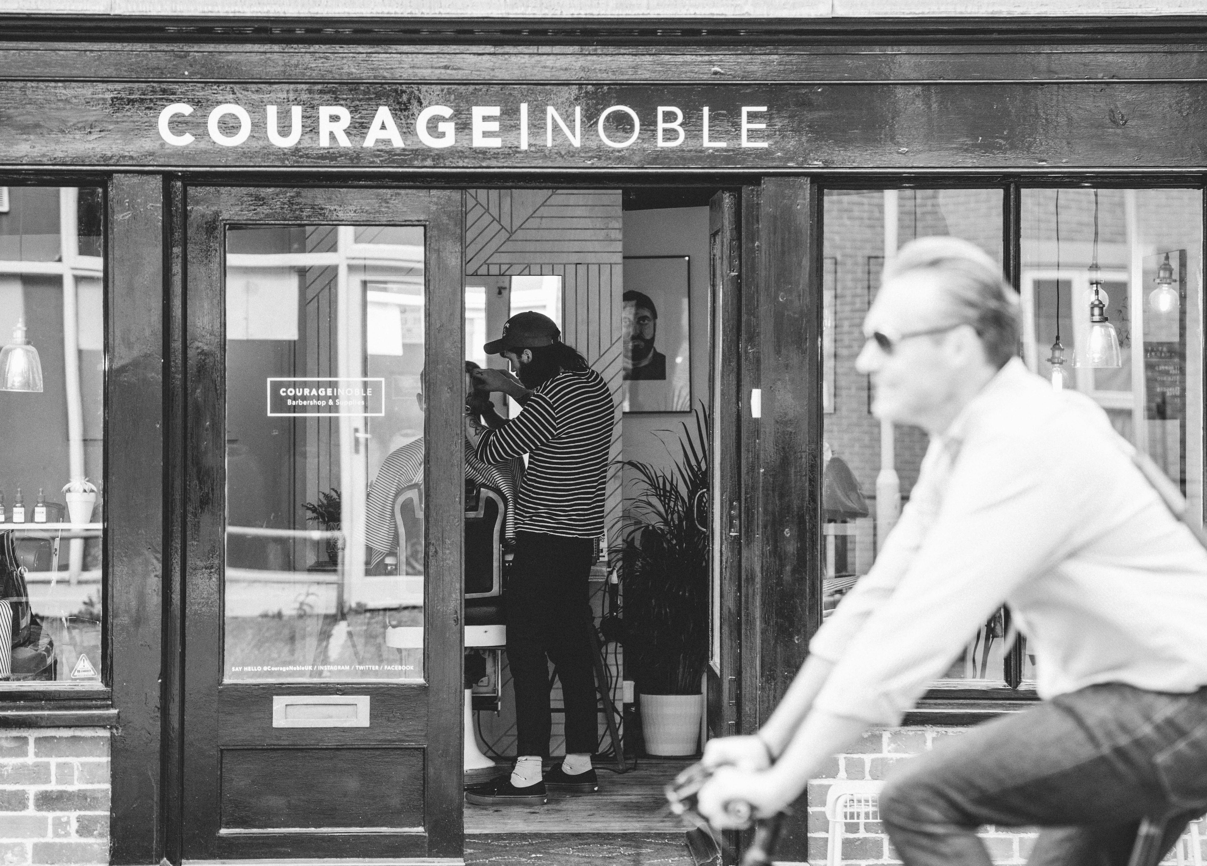 Exterior of Courage Noble | King Street, Norwich, England, GB with a cyclist passing by the barbershop.
