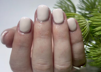 Close-up of a chic cream manicure at Snatched Cosmetics, Boksburg, Gauteng, ZA, with green foliage backdrop.