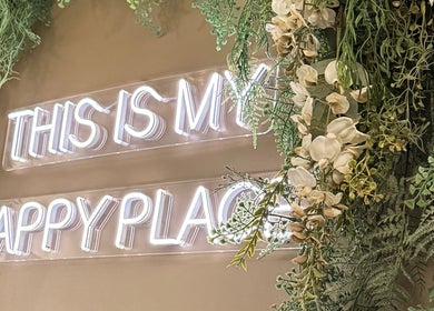 Neon sign 'This is my happy place' at Mirrored by Melissa | Root Rituals, Webster, New York, US amidst greenery.