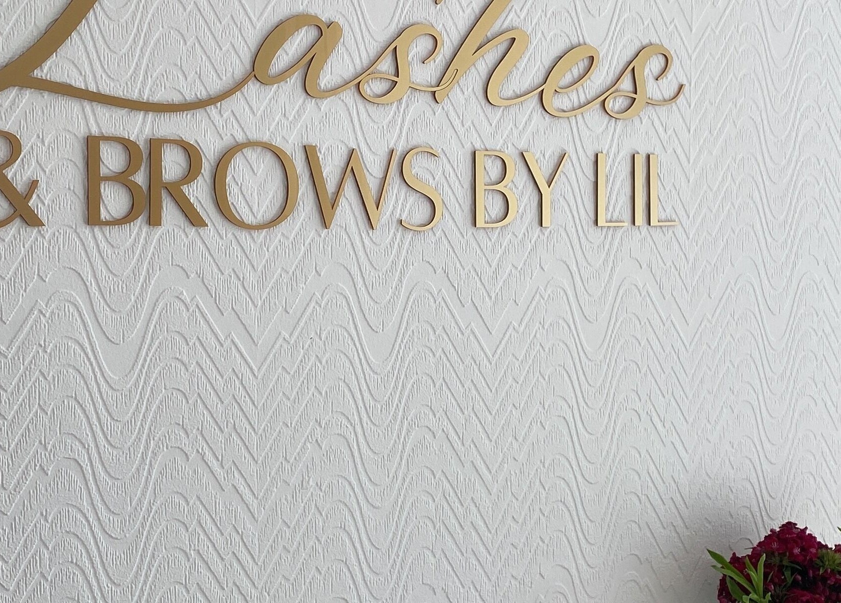 Gold sign of Lashes & Brows By Lil on a textured wall in Hoddesdon, England, GB.