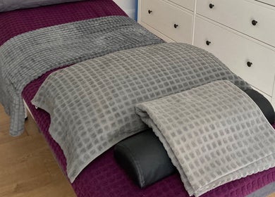Massage bed at The Relaxation Room Leixlip, Leixlip, County Kildare, IE with soft gray and purple linens.