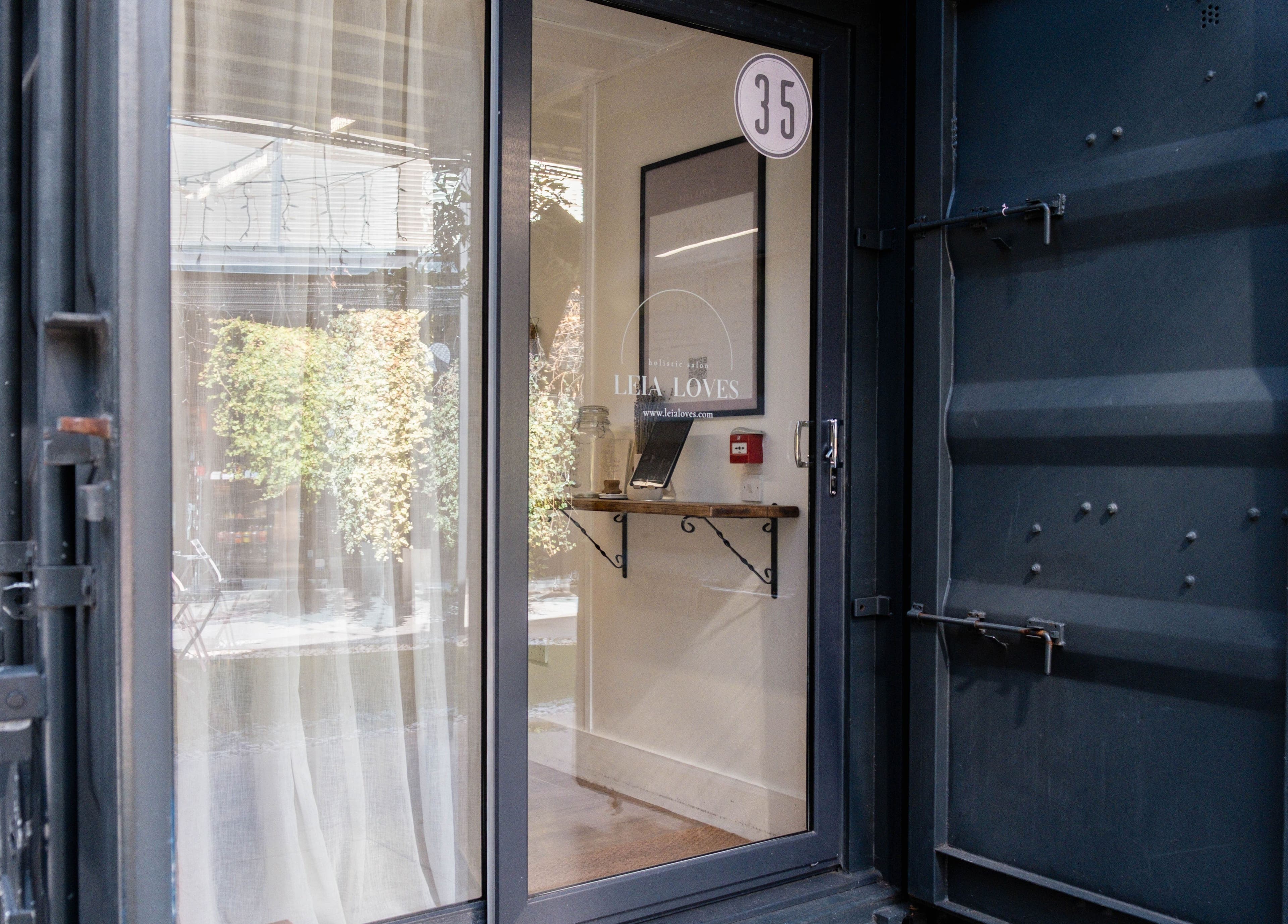 Entrance to Leia Loves, a serene beauty venue in London, England, GB with glass door and leafy decor.