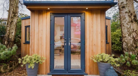 The Beauty Shack in Failand, England, GB features a cozy wooden exterior with glass doors surrounded by greenery.