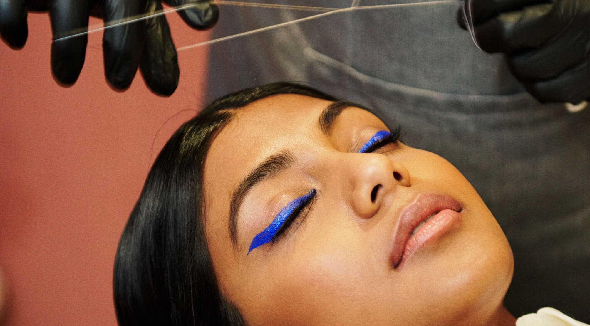 Eyebrow threading at Iris Avenue, London, England, GB with vibrant blue eyeliner accent on woman.