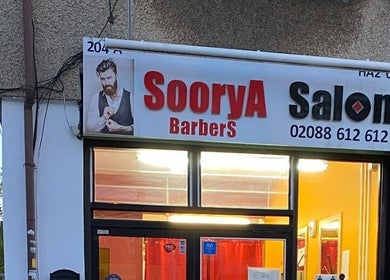 Exterior view of Soorya Barbers located in Harrow, England, GB at dusk with illuminated sign.