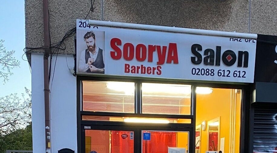 Exterior view of Soorya Barbers located in Harrow, England, GB at dusk with illuminated sign.