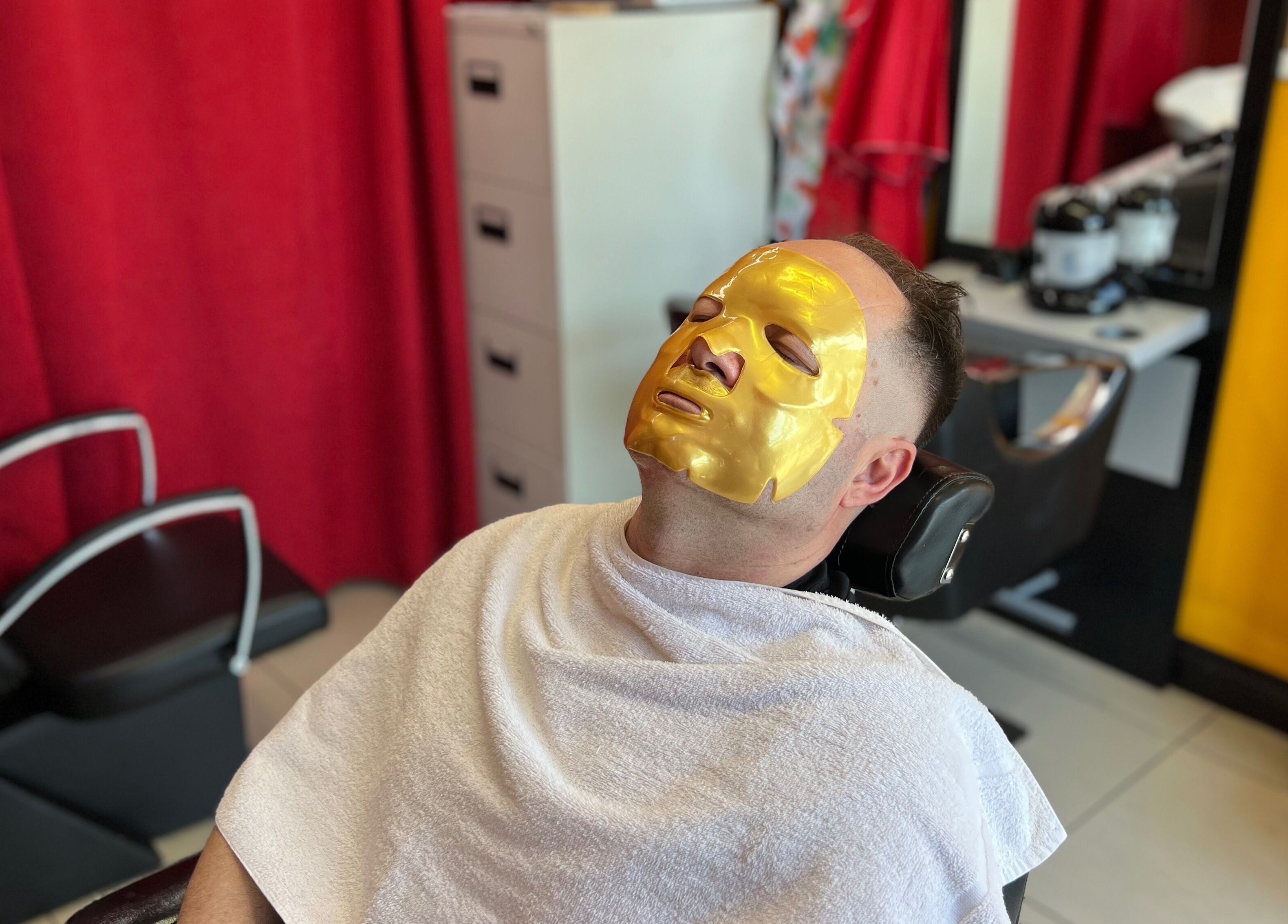 Client at Soorya Barbers in Harrow, England, GB enjoying a rejuvenating gold facial mask treatment.